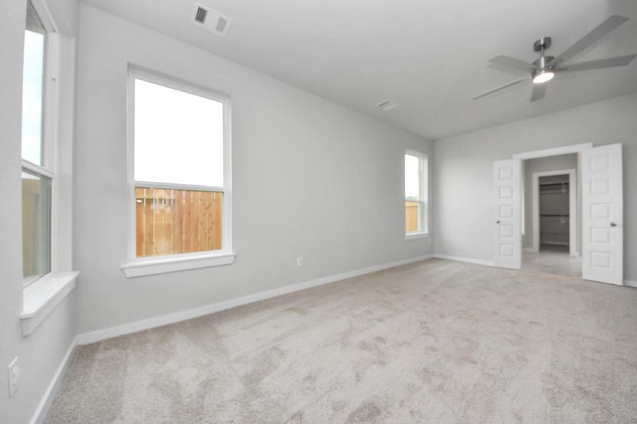 Escape and relax in the exquisite primary suite, a haven to unwind after a long day. The spacious room, located on first floor, boasts plush carpeting, soothing paint tones, high ceilings, and expansive windows adorned with privacy blinds. Sample photo of completed home with similar floor plan. Actual colors and selections may vary.