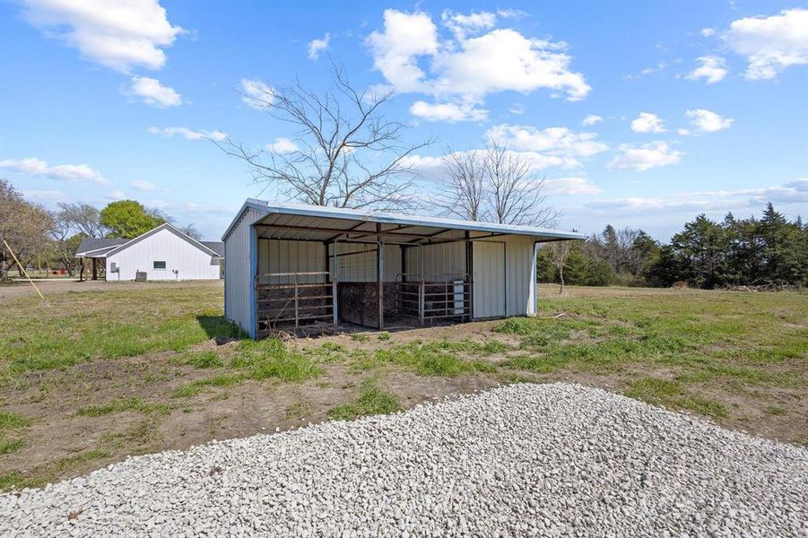 The property features an open-sided metal structure, a expansive grassy area, and a large pile of light-colored gravel