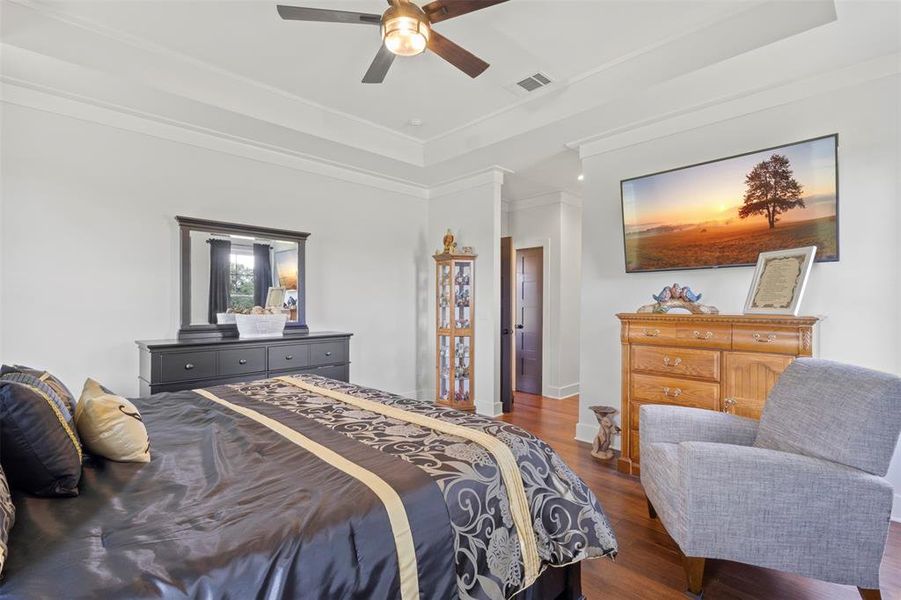 Elegant bedroom retreat featuring rich hardwood flooring, tray ceiling detail, elevated trim work, and serene acreage views—offering a refined blend of comfort, privacy, and timeless country luxury.