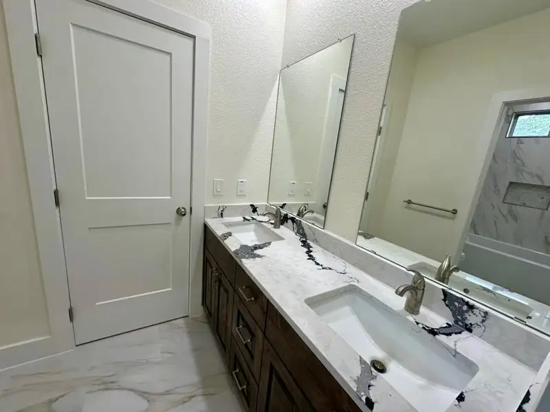 Bathroom featuring double vanity, light marble finish flooring, and a textured wall