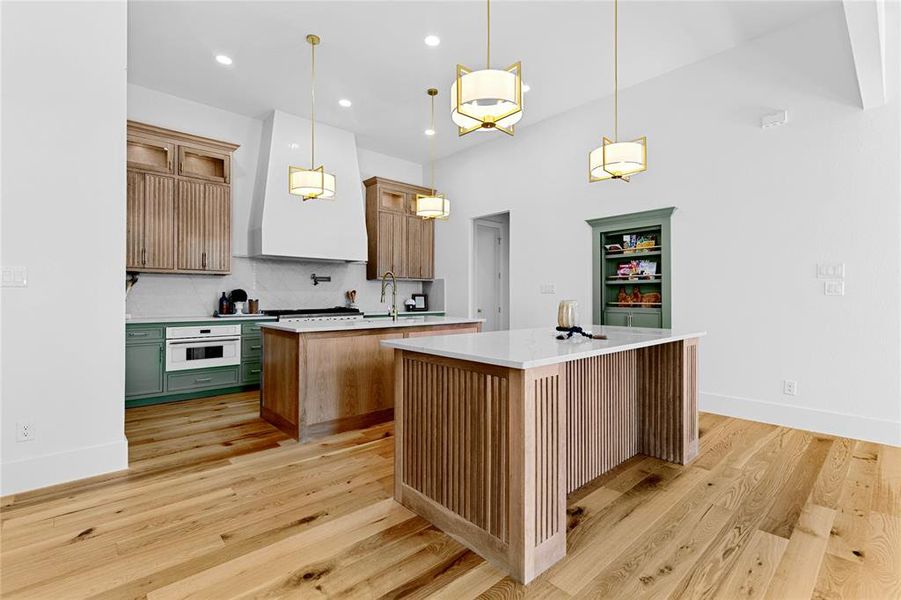 Kitchen featuring pendant lighting, custom exhaust hood, quartz backsplash, light quartz counters, and light wood finished floors. Kitchen featuring pendant lighting, custom exhaust hood, quartz backsplash, light quartz counters, and light wood finished floors.