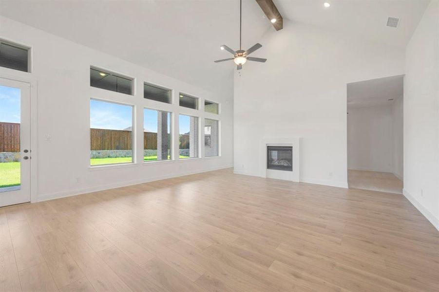 Spacious living area featuring light wood-finish flooring, a contemporary fireplace, and a vaulted ceiling with exposed beams Spacious living area featuring light wood-finish flooring, a contemporary fireplace, and a vaulted ceiling with exposed beams