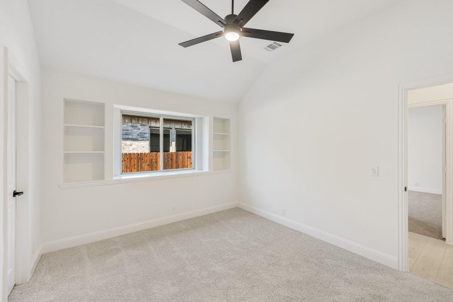 Empty bedroom with vaulted ceiling, ceiling fan, built-in shelves, and carpet flooring