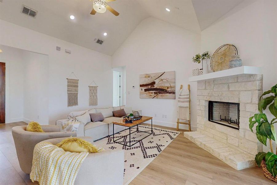 Living room featuring light wood-type flooring, high vaulted ceiling, ceiling fan, and a stone fireplace