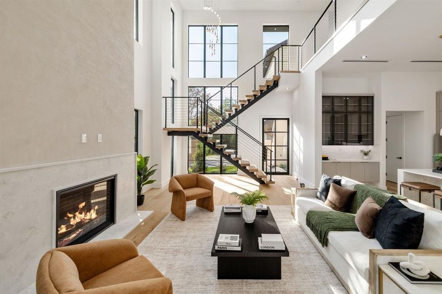 Two-story living area featuring a prominent staircase with metal railings and open treads, a fireplace with a light-toned surround, expansive windows, wood-finish flooring, and a built-in wet bar with dark-framed cabinetry