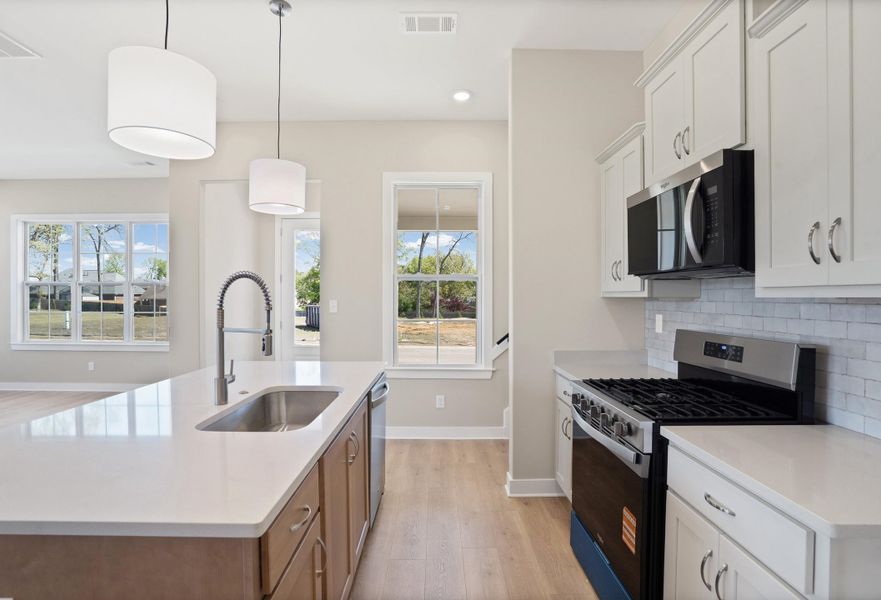 Dual tone kitchen featuring stainless steel appliances, a center island with sink, hanging light fixtures, light wood-style floors, and decorative backsplash