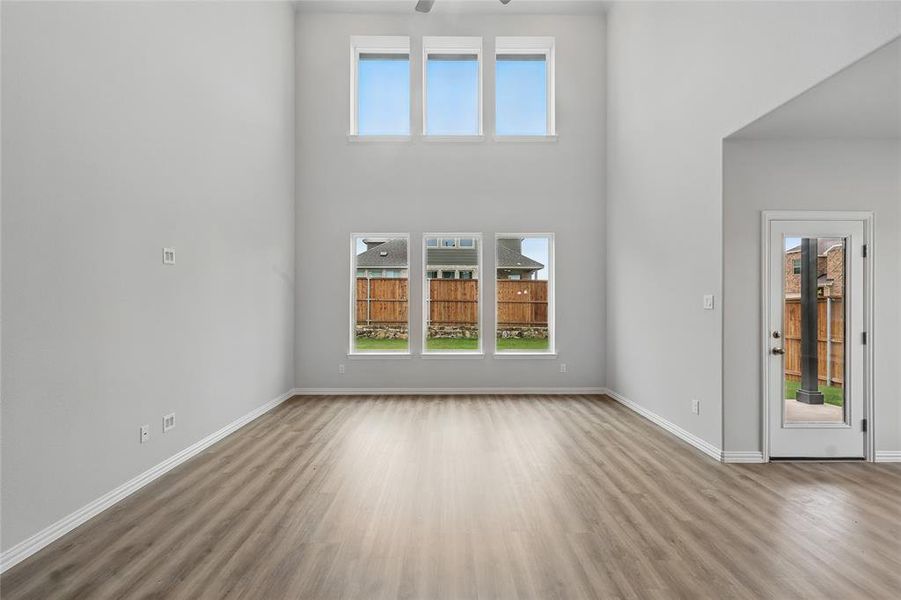 Unfurnished living room featuring wood finished floors, baseboards, a towering ceiling, and a ceiling fan Unfurnished living room featuring wood finished floors, baseboards, a towering ceiling, and a ceiling fan