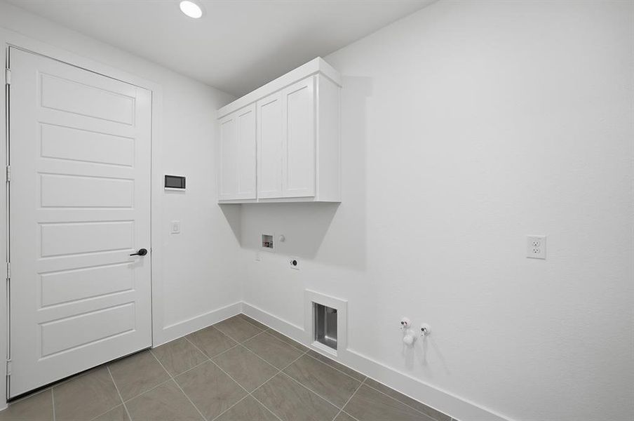 Laundry area featuring gas dryer hookup, cabinet space, dark tile patterned floors, washer hookup, and electric dryer hookup Laundry area featuring gas dryer hookup, cabinet space, dark tile patterned floors, washer hookup, and electric dryer hookup