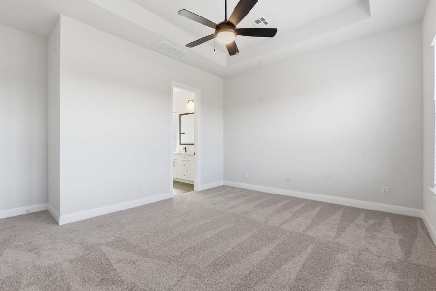 Unfurnished bedroom featuring a tray ceiling, light carpet, a ceiling fan, and connected bathroom
