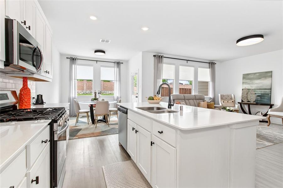 Open concept living space featuring a kitchen with white cabinetry, stainless steel appliances, and a central island with a sink, dining area with a round table, and a living area with large windows