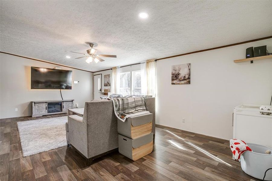 Living room with a textured ceiling, dark wood-type flooring, a fireplace, vaulted ceiling, and ceiling fan