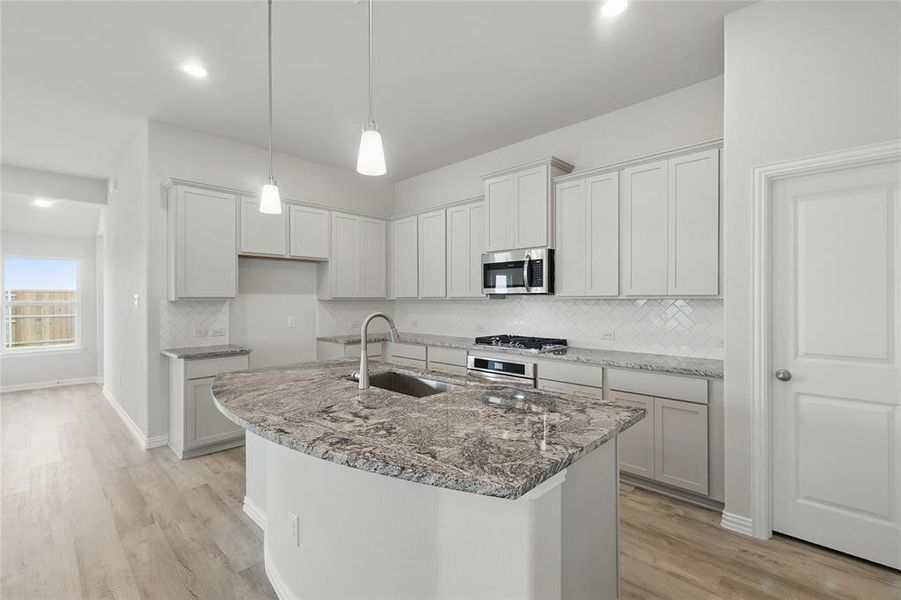 Kitchen with a sink, stainless steel appliances, decorative backsplash, light wood-style floors, and a kitchen island with sink Kitchen with a sink, stainless steel appliances, decorative backsplash, light wood-style floors, and a kitchen island with sink