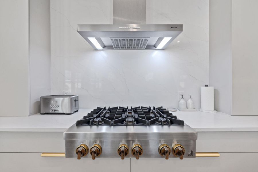 Kitchen view of stainless steel gas cooktop, decorative backsplash, and light stone counters