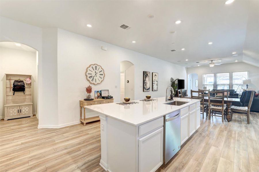 Kitchen with arched walkways, stainless steel dishwasher, light wood-style floors, recessed lighting, and a kitchen island with sink