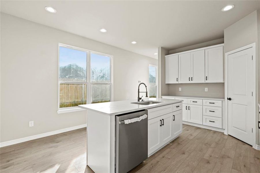 Kitchen with white cabinets, dishwasher, an island with sink, and sink