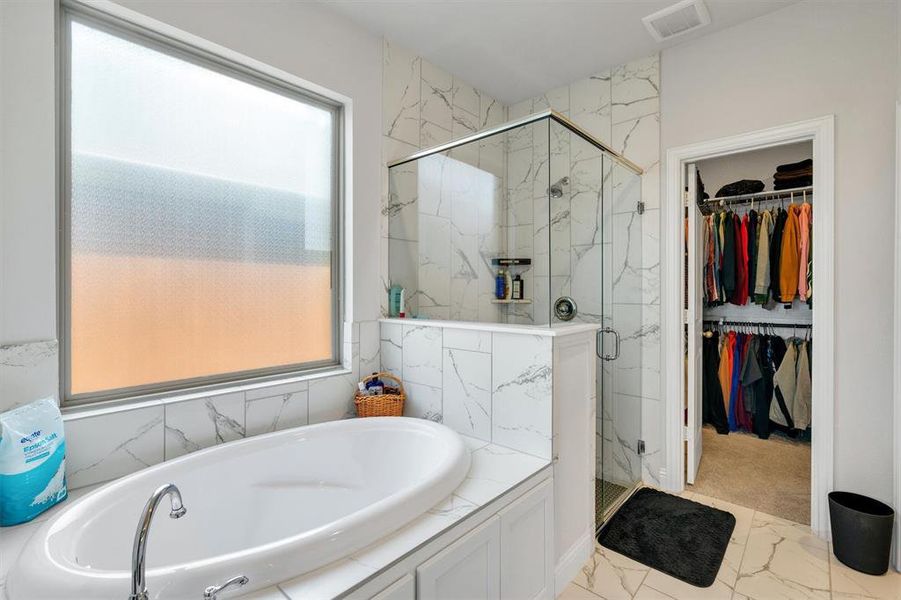 Freestanding soaking tub with polished chrome faucet, surrounded by marbled tile accents