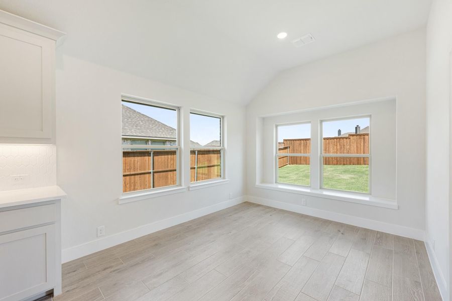 Empty dining or breakfast room with vaulted ceiling, light wood-look floors, and large windows overlooking backyard