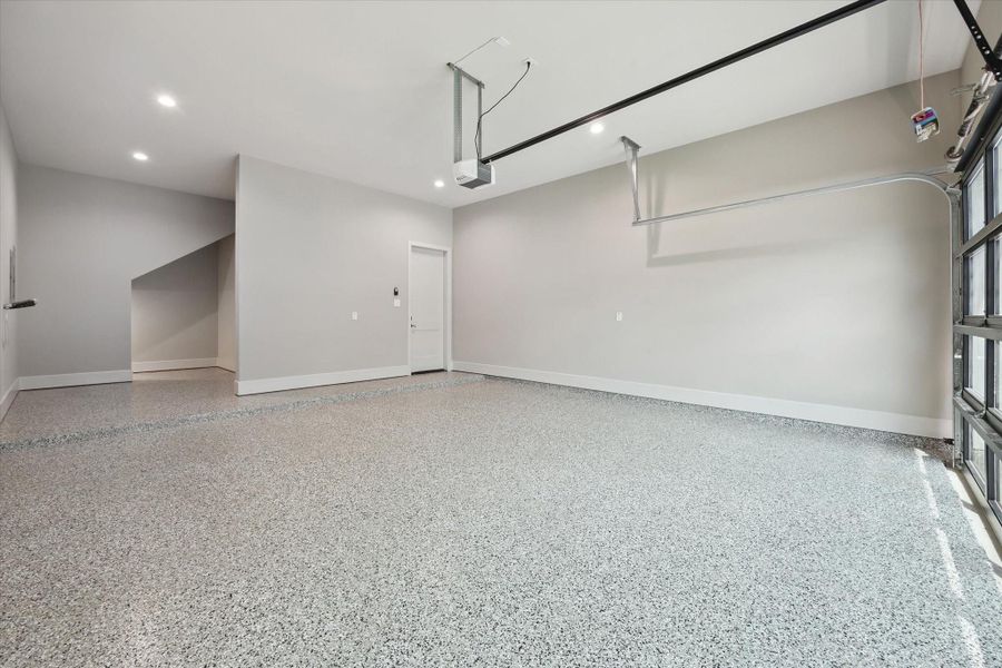 The garage showcases a sleek and durable epoxy floor, providing both style and easy maintenance. A modern glass and metal garage door enhances curb appeal, while ample storage space adds functionality—and the garage is wired for an EV charger, making it both practical and future-ready.