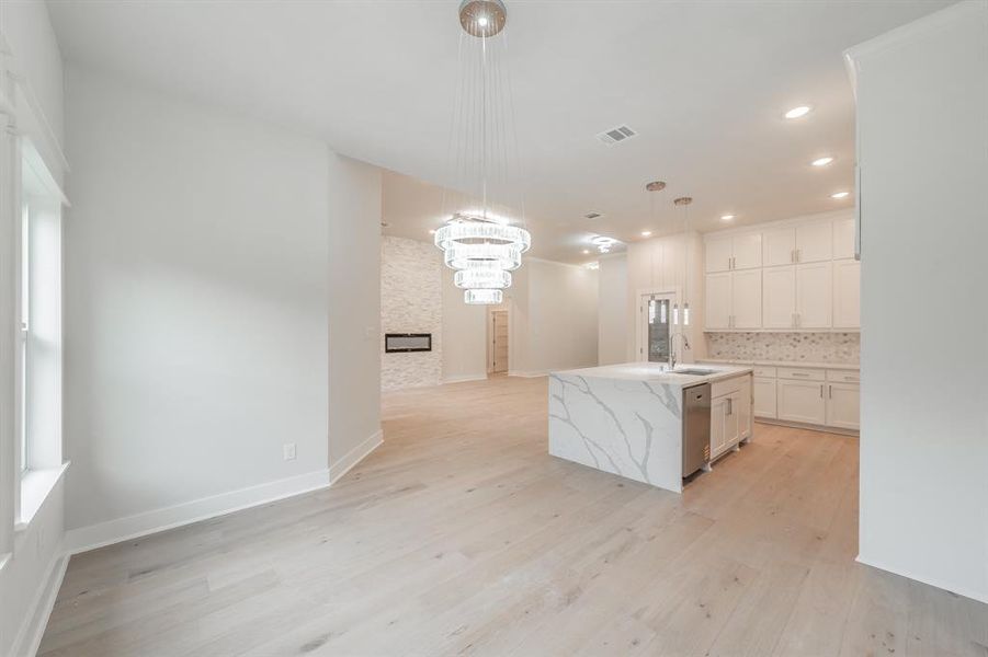 Kitchen with decorative light fixtures, white cabinetry, a kitchen island with sink, light stone counters, and backsplash