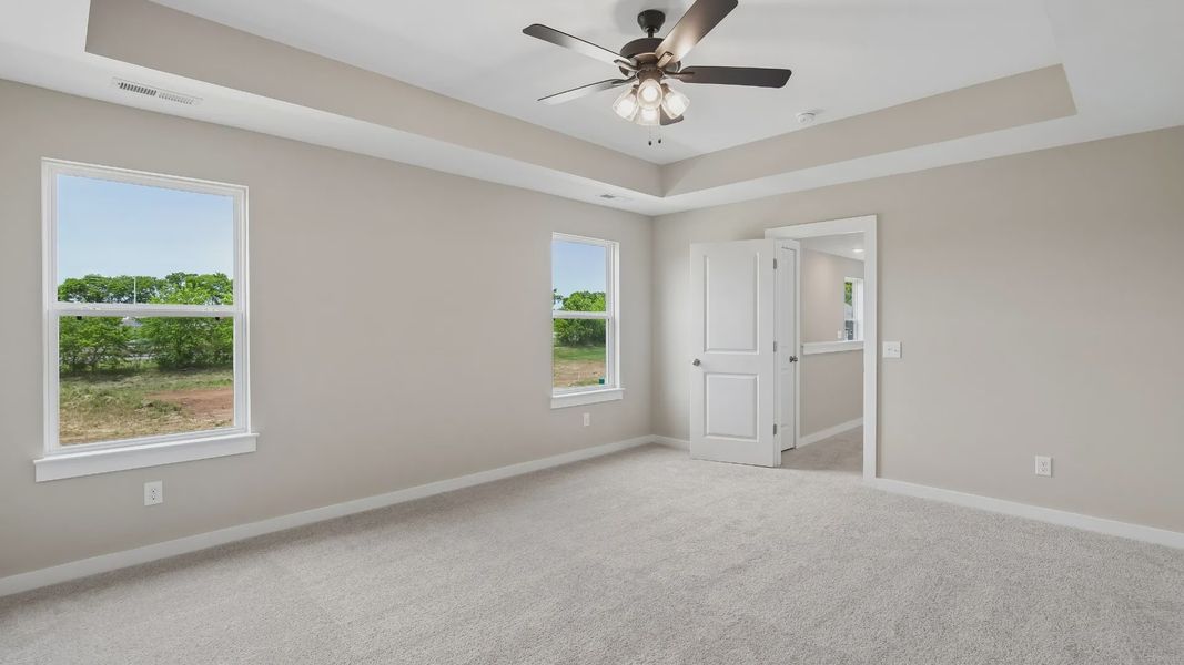 Bedroom with tray ceiling, windows, and en-suite primary bathroom Bedroom with tray ceiling, windows, and en-suite primary bathroom