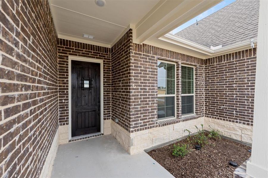 Doorway to property featuring brick siding, roof with shingles, and covered porch