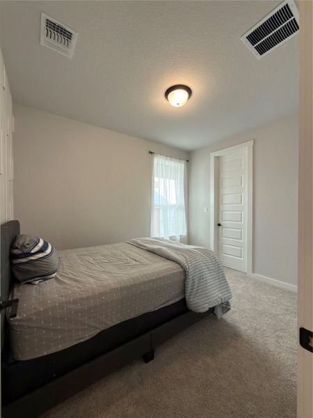 Carpeted room featuring a ceiling-mounted light fixture, a window with sheer curtains, a paneled door with a dark handle, and light-toned walls