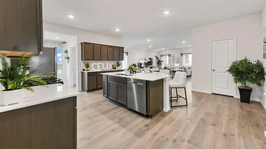 Spacious kitchen featuring an expansive center island with a stainless steel dishwasher, wood-finish cabinetry, light-toned countertops, a built-in oven, and wood-finish flooring Spacious kitchen featuring an expansive center island with a stainless steel dishwasher, wood-finish cabinetry, light-toned countertops, a built-in oven, and wood-finish flooring