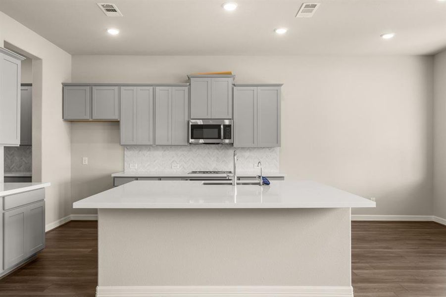 This light and bright kitchen features a large quartz island, cool toned cabinets, a large sink overlooking your family room, recessed lighting, and beautiful backsplash.