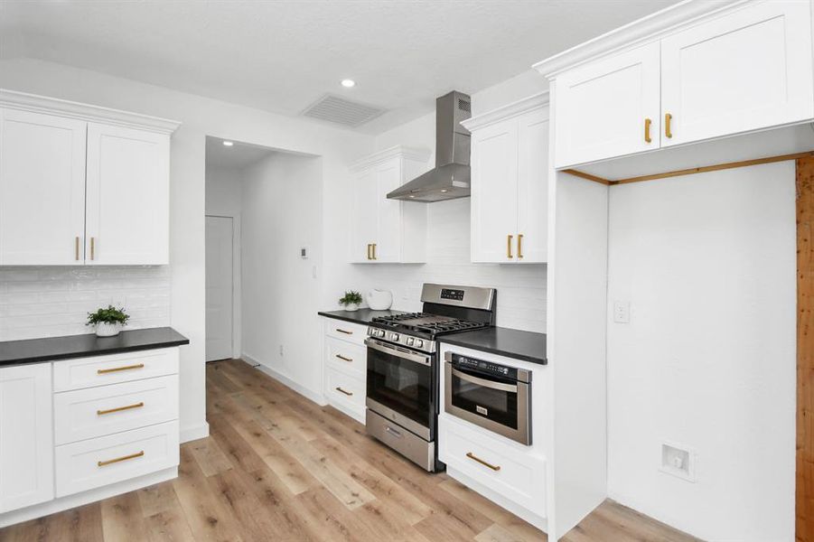 This is a modern kitchen with white cabinetry, stainless steel appliances, and a subway tile backsplash. It features a gas range and a built-in microwave, with sleek hardware and a spacious layout that opens into a dining area.