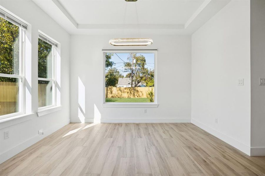 Unfurnished dining area featuring light wood-style flooring and a raised ceiling