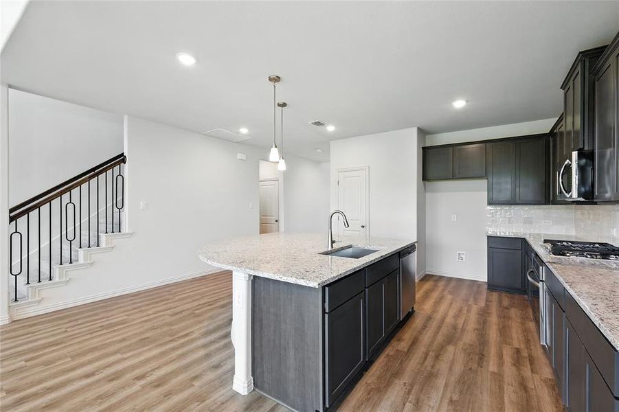 Kitchen with light stone counters, pendant lighting, dark wood-style floors, a center island with sink, and backsplash