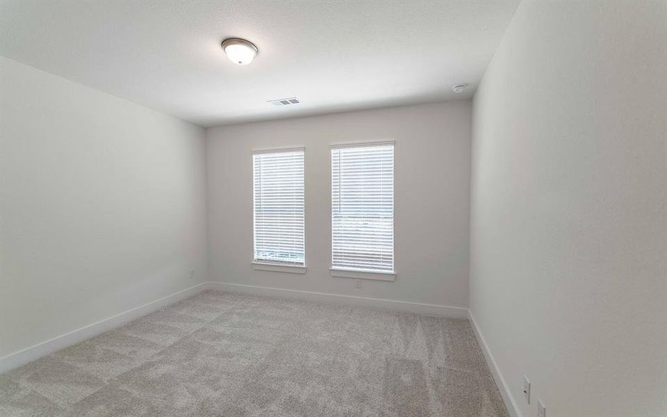 Neutral tone walls featuring two windows with horizontal blinds, overhead flush mount lighting, and grey patterned carpeting