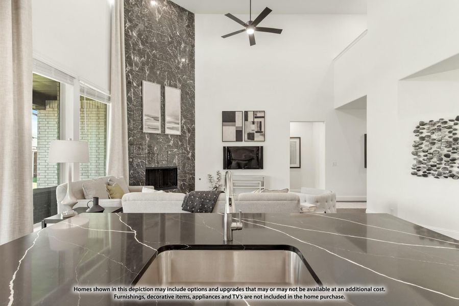 Open-concept living area with dark marble fireplace wall, high ceilings, ceiling fan, and dark stone kitchen countertop in foreground Open-concept living area with dark marble fireplace wall, high ceilings, ceiling fan, and dark stone kitchen countertop in foreground