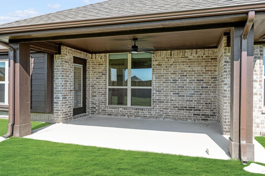 Covered back patio with ceiling fan, concrete floor, and brick exterior wall adjacent to green lawn Covered back patio with ceiling fan, concrete floor, and brick exterior wall adjacent to green lawn