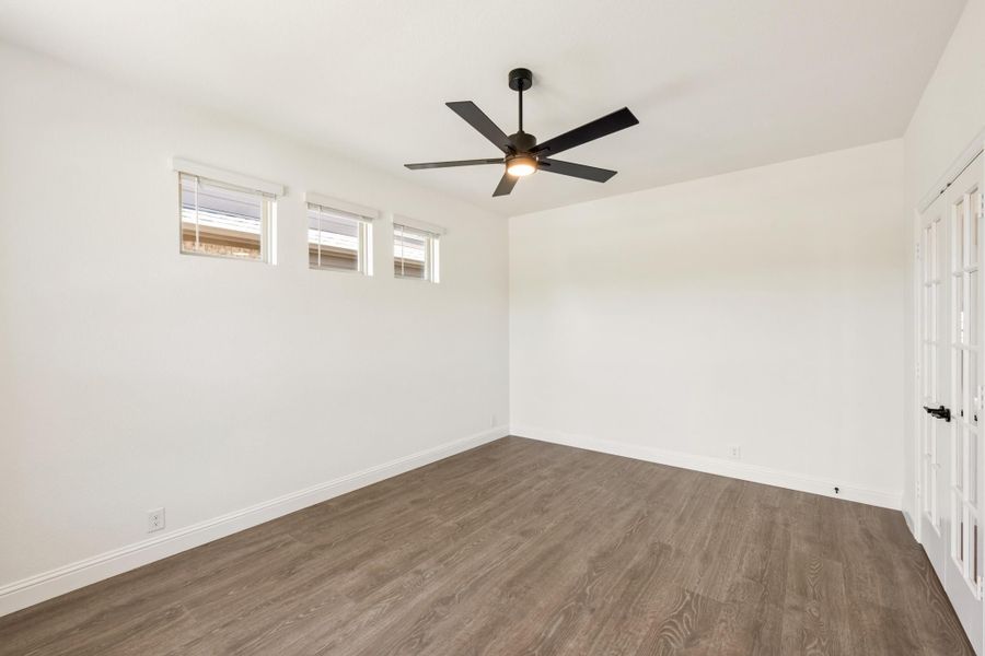 Empty room with dark wood floors, black ceiling fan, white walls, and three small windows