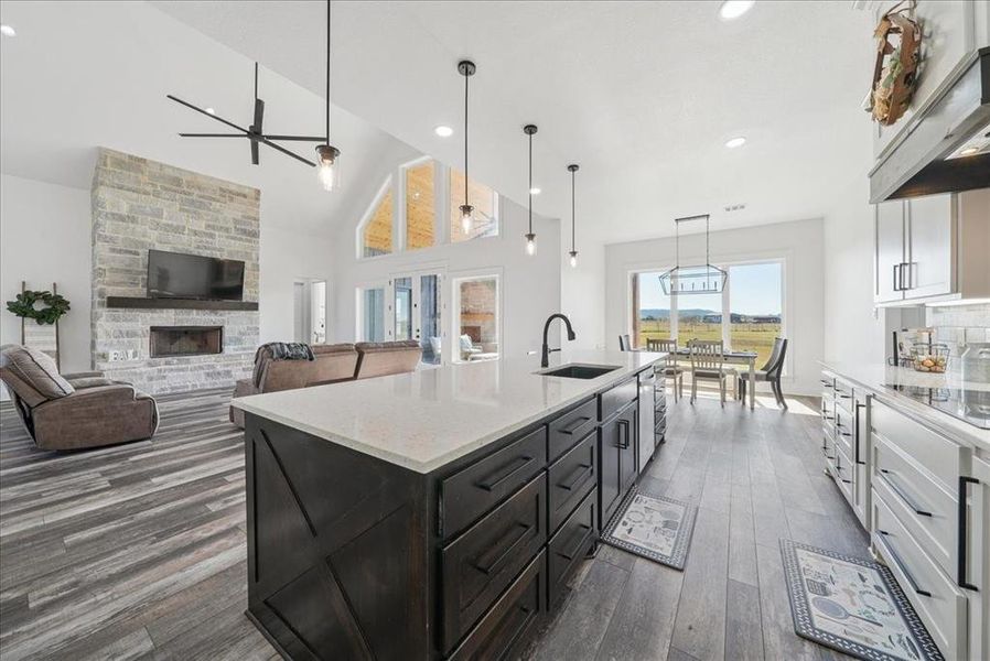 Kitchen with pendant lighting, light stone counters, a stone fireplace, white cabinets, and dark wood-style flooring