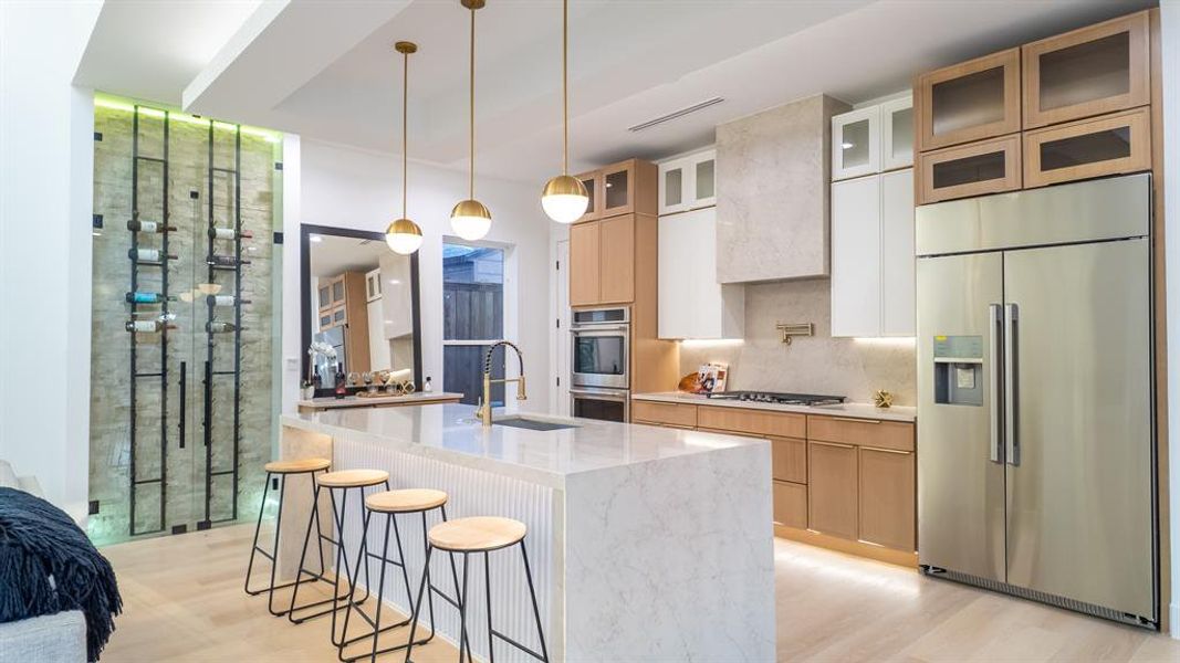 Kitchen with stainless steel appliances, pendant lighting, white cabinets, light wood finished floors, and a kitchen bar