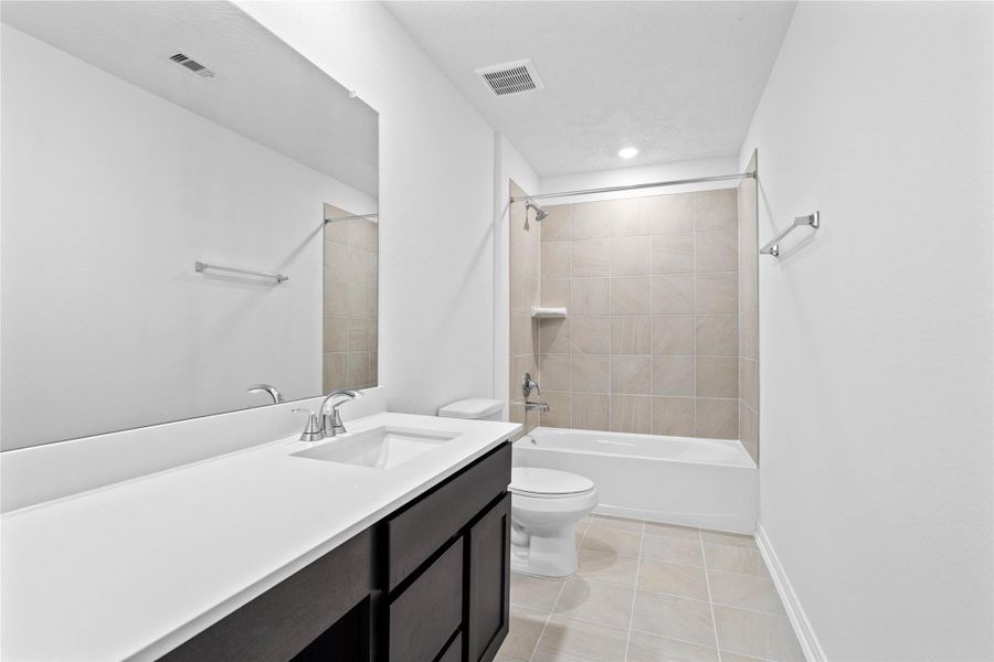 The secondary bathroom showcases tile flooring, a bath/shower combo with Daltile tile surround, a vanity with knee space and stunning light countertop, a mirror, sleek fixtures, and contemporary finishes throughout.