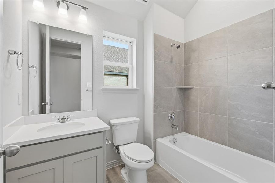 Full bathroom featuring a single vanity with a white countertop and base cabinetry, chrome fixtures, a rectangular mirror, and a bathtub with light gray tile surround Full bathroom featuring a single vanity with a white countertop and base cabinetry, chrome fixtures, a rectangular mirror, and a bathtub with light gray tile surround