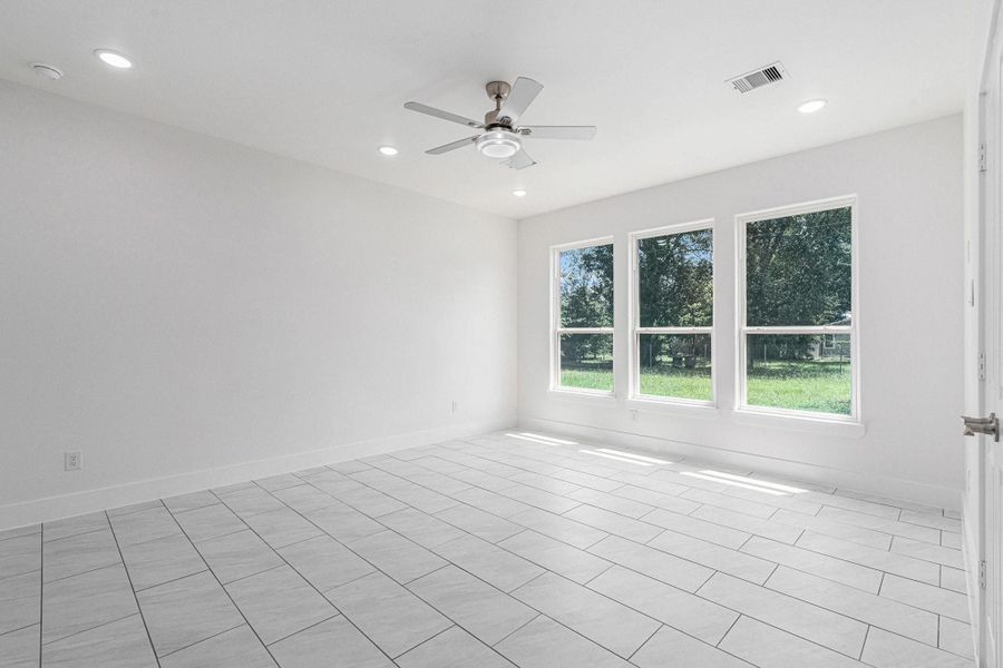 This is a bright, spacious room with large windows offering a view of a green yard. It features tiled floors, recessed lighting, and a ceiling fan, providing a modern and airy feel. This is a bright, spacious room with large windows offering a view of a green yard. It features tiled floors, recessed lighting, and a ceiling fan, providing a modern and airy feel.