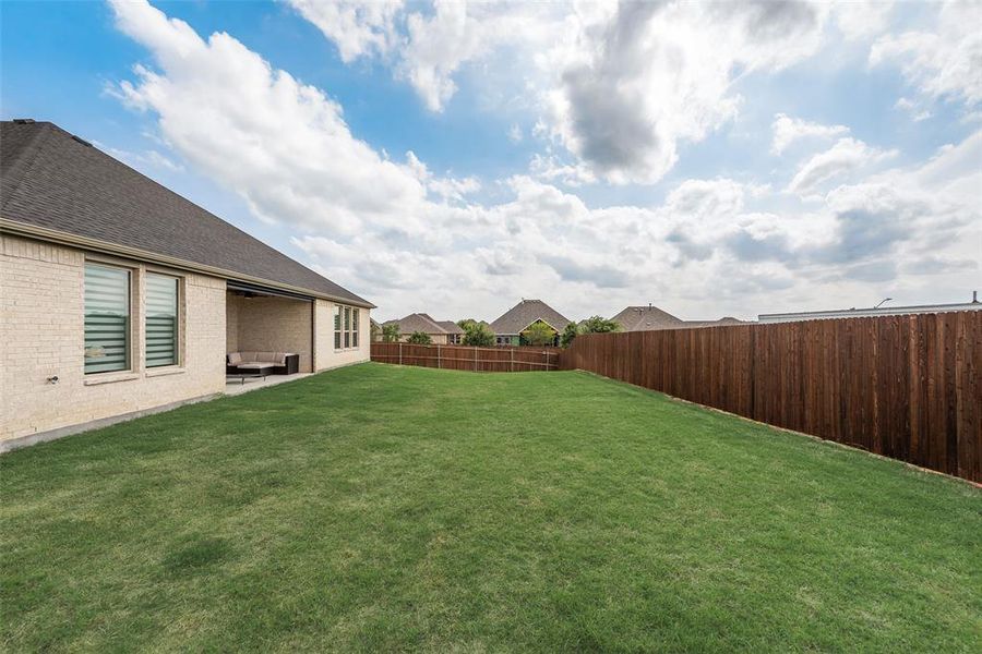 Spacious backyard featuring a manicured lawn, a full privacy fence, and a covered patio area