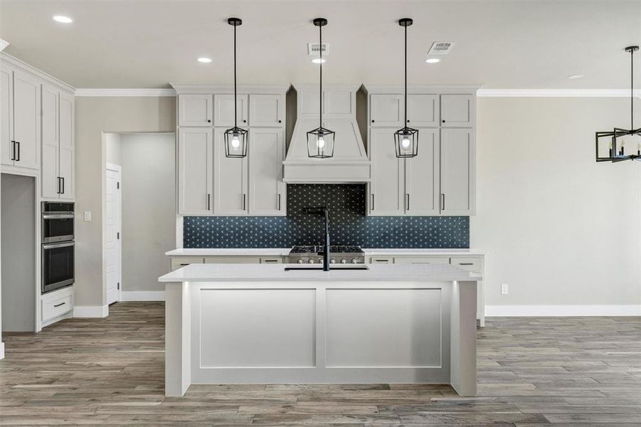 Kitchen featuring pendant lighting, an island with sink, custom exhaust hood, and white cabinets