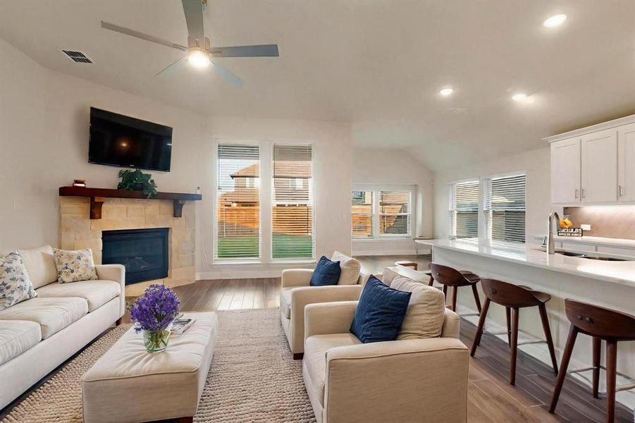 Living room with light wood finished floors, recessed lighting, a tiled fireplace, vaulted ceiling, and ceiling fan