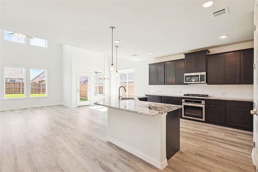 Kitchen with light wood-type flooring, backsplash, appliances with stainless steel finishes, decorative light fixtures, and sink