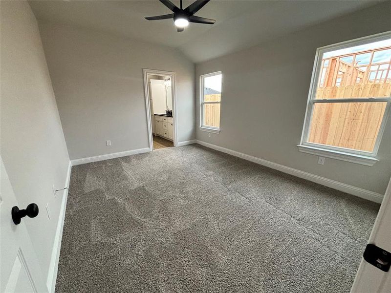 Unfurnished bedroom with light colored carpet, lofted ceiling, ensuite bathroom, and ceiling fan