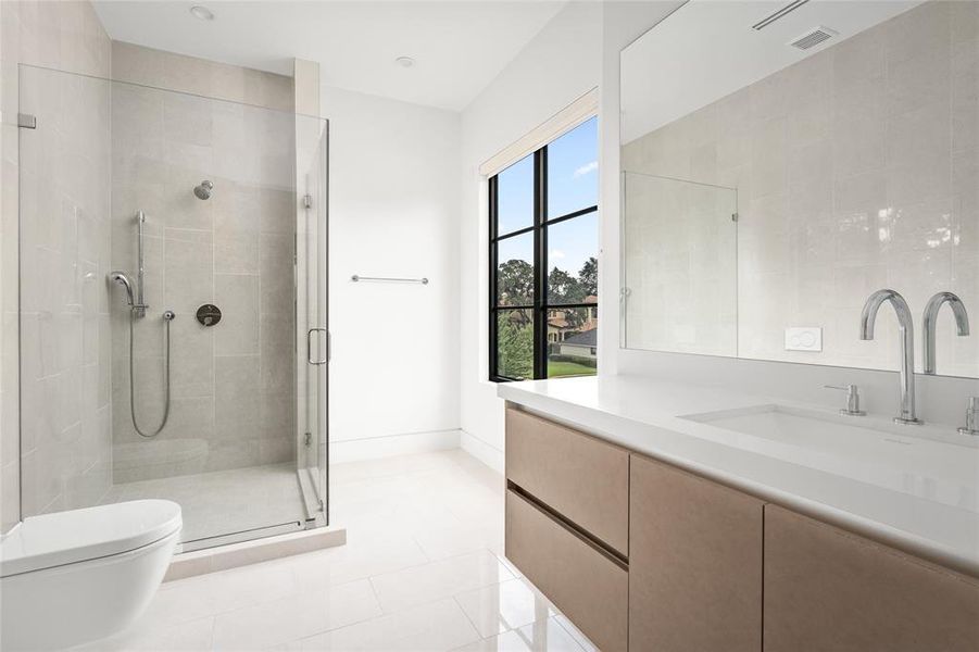 This secondary bathroom boasts a sleek, minimalist design with clean lines and an abundance of natural light. The spacious glass-enclosed shower features modern fixtures and light-colored tile, while the floating vanity with a pristine white countertop with an integrated sink provides a streamlined, contemporary look.