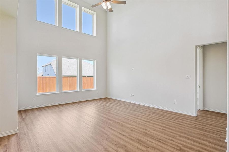 Unfurnished living room featuring ceiling fan, light hardwood / wood-style floors, and a high ceiling