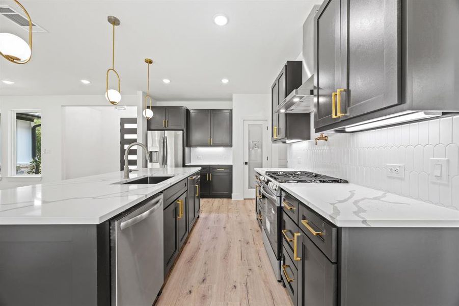 Kitchen featuring stainless steel appliances, a sink, light wood-type flooring, backsplash, and light stone counters Kitchen featuring stainless steel appliances, a sink, light wood-type flooring, backsplash, and light stone counters