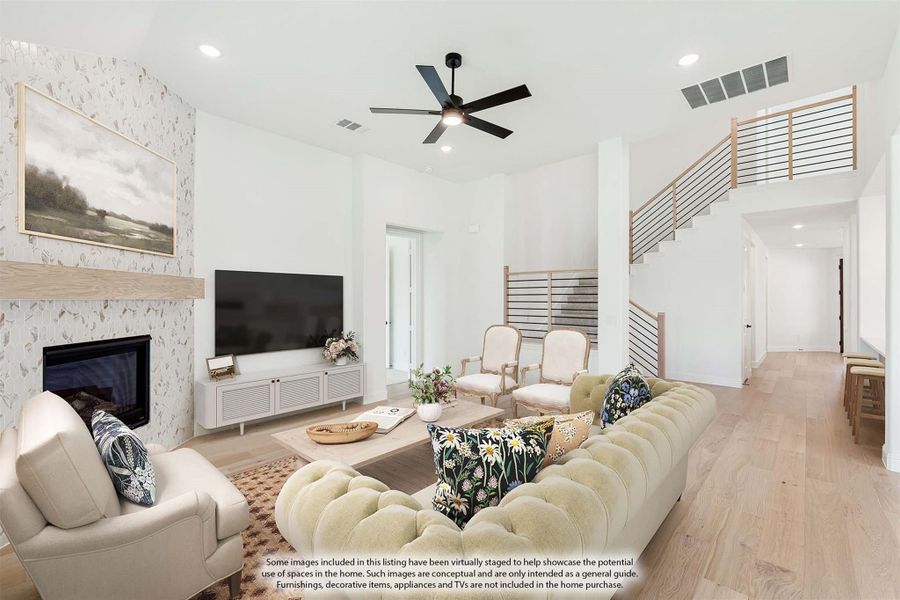 Open living room with high ceilings, fireplace, ceiling fan, and staircase with light wood floors