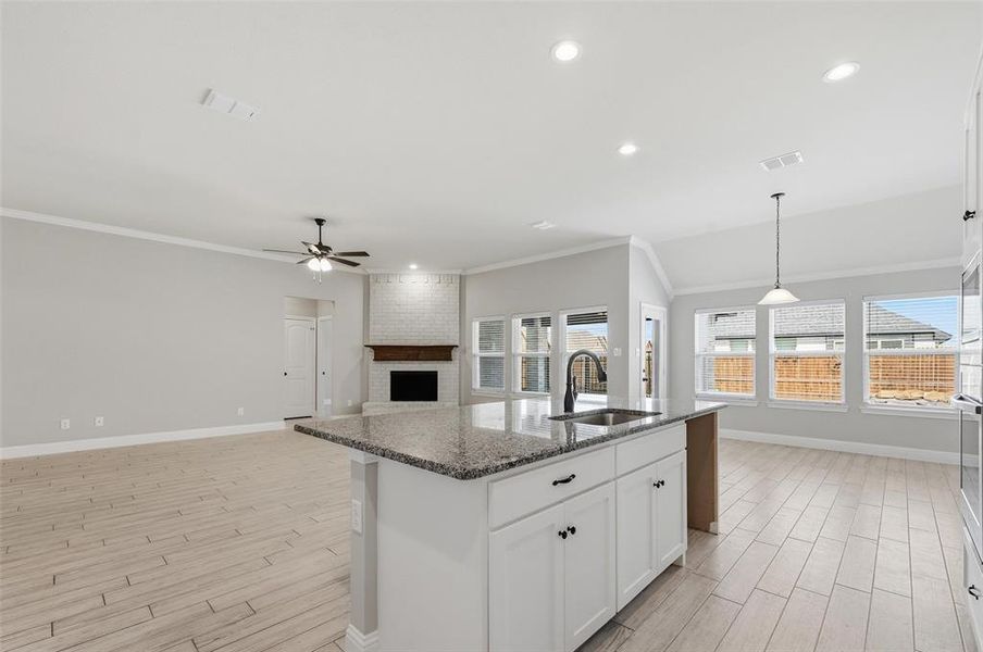 Kitchen featuring white cabinets, wood finish floors, a fireplace, dark stone counters, and ornamental molding Kitchen featuring white cabinets, wood finish floors, a fireplace, dark stone counters, and ornamental molding